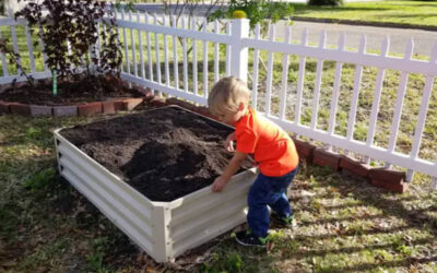Child and raised-bed planted by white picket fence