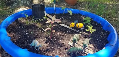 Blue kiddie pool turned into kid's garden with toy trucks and dinosaurs in it